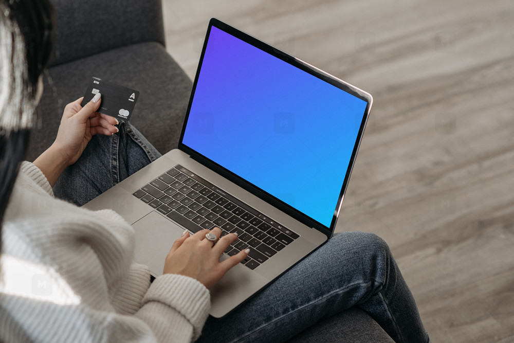 Mockup of female user on a couch shopping online with her grey MacBook and a MasterCard in hand