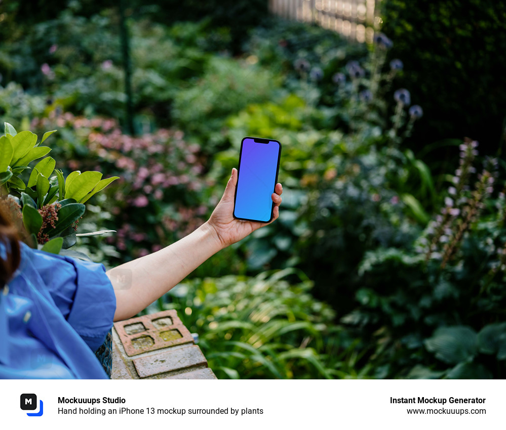 Hand holding an iPhone 13 mockup surrounded by plants