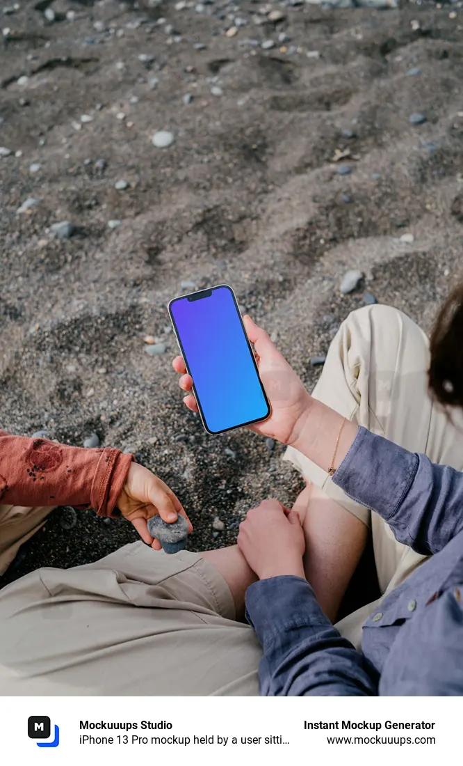iPhone 13 Pro mockup held by a user sitting on sand