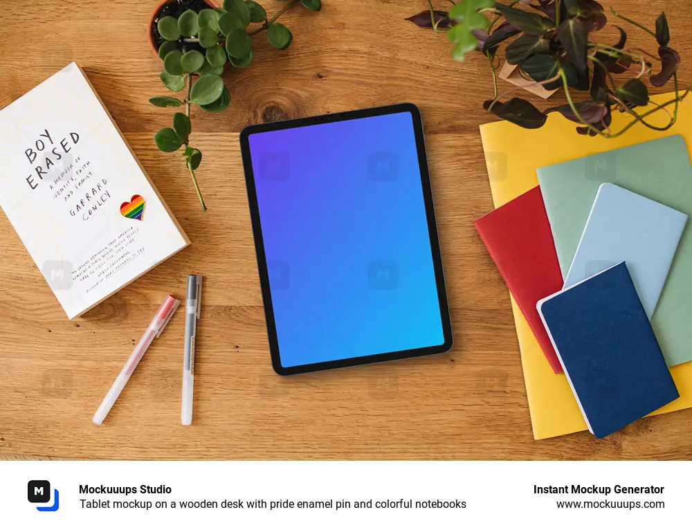 Tablet mockup on a wooden desk with pride enamel pin and colorful notebooks