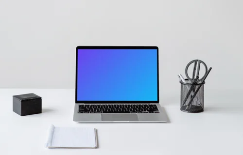 MacBook mockup on a white table with a notebook in front of it