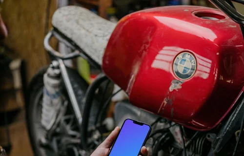 Man holding up an iPhone 13 Pro mockup beside a motorcycle