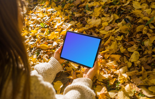 Manos femeninas sosteniendo un iPad Air entre las hojas mockup