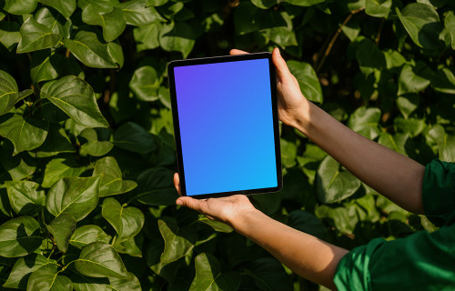 Female holding an iPad Air mockup in front of plant leaves