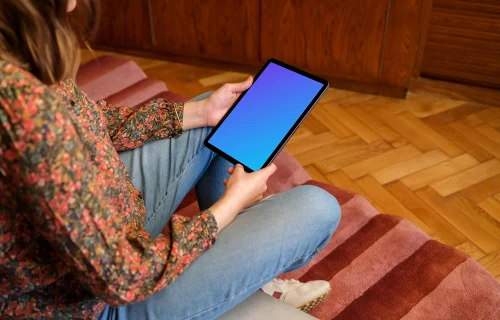 Female holding iPad mockup against a wooden background in the lounge