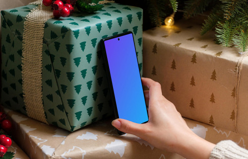 Mano sosteniendo un teléfono mockup bajo el árbol de Navidad