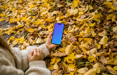 Mano sosteniendo un iPhone entre las hojas otoñales mockup