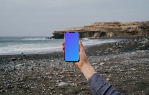 iPhone 13 Pro mockup held by a user against the ocean