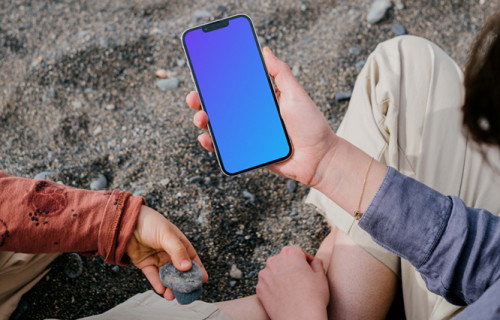 iPhone 13 Pro mockup held by a user sitting on sand