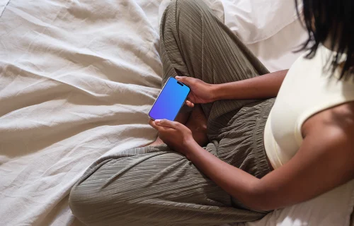 iPhone 15 Pro mockup in a woman's hands on cozy bedding