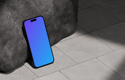 iPhone 16 mockup leaning against a rock on tiled floor