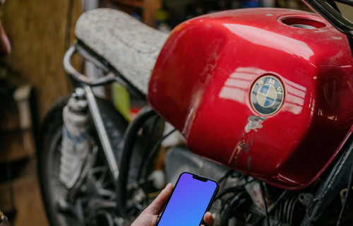 Man holding up an iPhone 13 Pro mockup beside a motorcycle