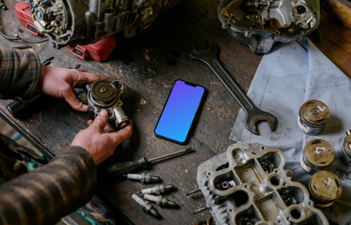 Hombre con un iPhone 13 Pro mockup sobre una mesa de trabajo mecánica