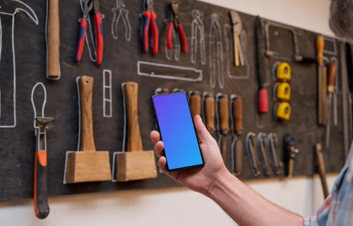 Mechanic holding a phone in front of a wall with tools