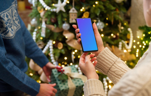 Teléfono mockup en manos junto al árbol de Navidad