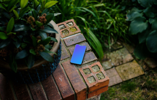 Phone mockup on a stone wall with plants in the background