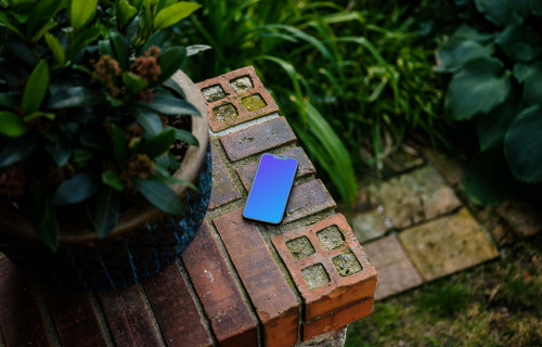 Teléfono mockup en un muro de piedra con plantas al fondo