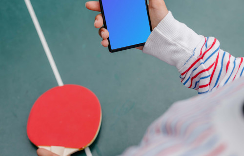 Woman hand holding a phone mockup while playing ping-pong