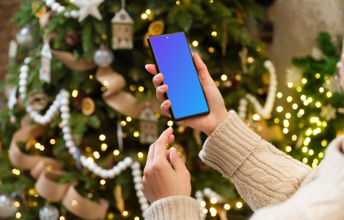 Woman hand holding a smartphone next to the Christmas tree