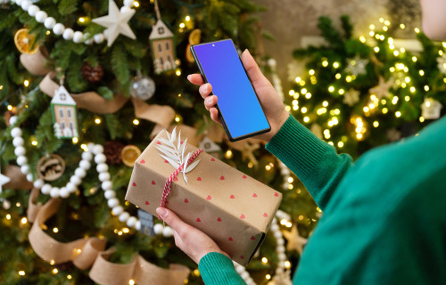 Mujer sosteniendo un teléfono y un regalo de Navidad