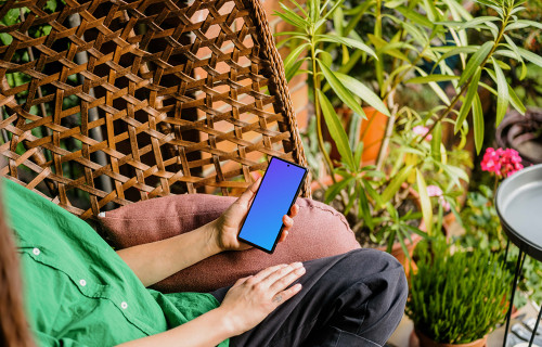 Mujer sosteniendo un teléfono mockup rodeada de plantas