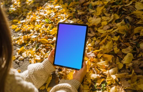 Mujer sosteniendo un iPad Air entre las hojas mockup