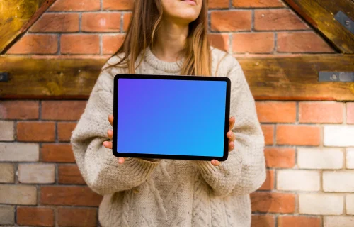 Mulher segurando um iPad em frente a uma parede de tijolos mockup