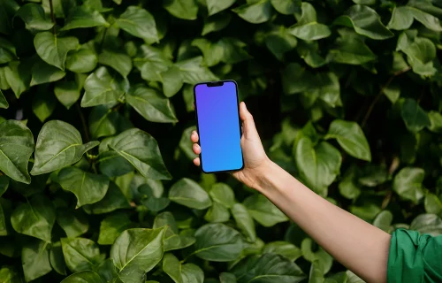 Femme tenant un iPhone 13 mockup devant des feuilles vertes