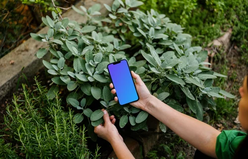 Mujer con un iPhone 13 mockup en un jardín verde