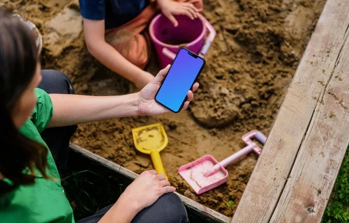 Femme tenant un iPhone 13 mockup dans un bac à sable