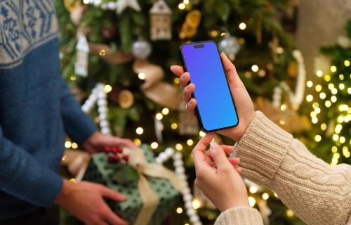 Mujer sosteniendo un iPhone mockup junto al árbol de Navidad