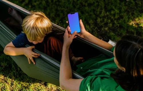 Mujer tumbada en una hamaca y escribiendo en un iPhone 13 mockup