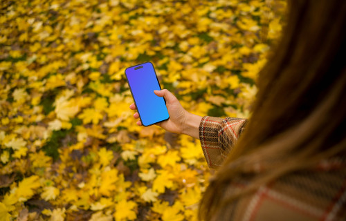 Woman scrolling on an iPhone 14 Pro in autumn season mockup