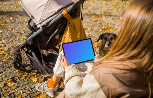 Mujer sentada sosteniendo un iPad Air en un parque temático otoñal mockup