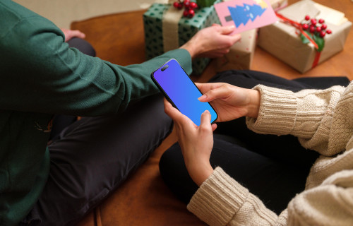 Mujer rodeada de regalos de Navidad tecleando en un teléfono mockup