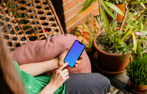 Mujer escribiendo en un iPhone 13 mockup en el jardín