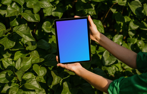Female holding an iPad Air mockup in front of plant leaves