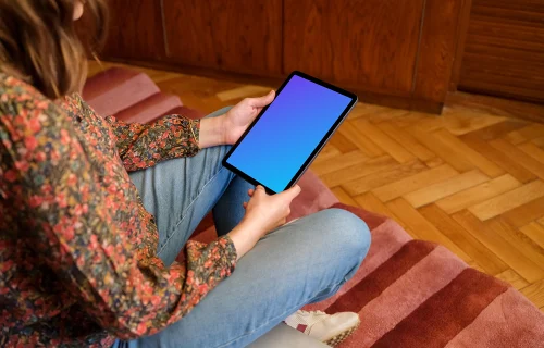 Female holding iPad mockup against a wooden background in the lounge