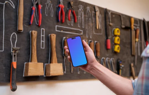 Hand holding an iPhone mockup in front of wall with tools