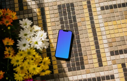 iPhone 13 mockup on a garden paving next to the flowers