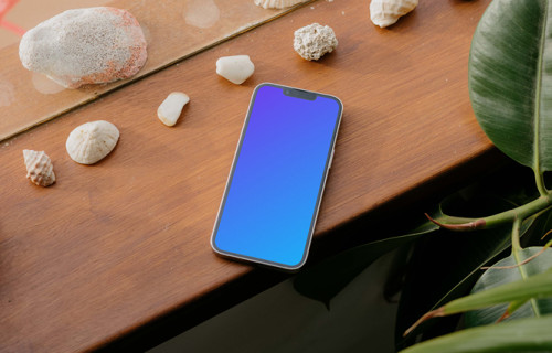iPhone 13 Pro mockup on a wooden table next to seashells