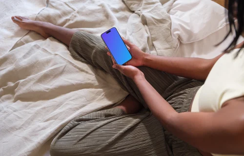 iPhone 15 Pro mockup in female hands on a cozy bed
