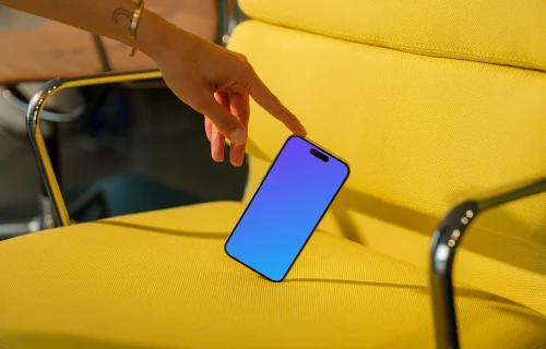 iPhone 15 Pro mockup with hand interaction on yellow chair