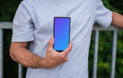 Man holding a phone mockup in front of a fence
