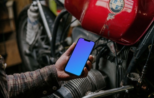Man holding up an iPhone 13 Pro mockup beside a motorcycle