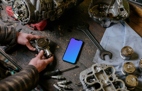 Man with an iPhone 13 Pro mockup on a mechanic worktable