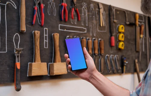 Mechanic holding a phone in front of a wall with tools