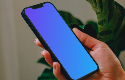 Person holding an iPhone 13 mockup with a plant in the background