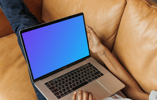 User on a leather sofa holding a MacBook Pro mockup