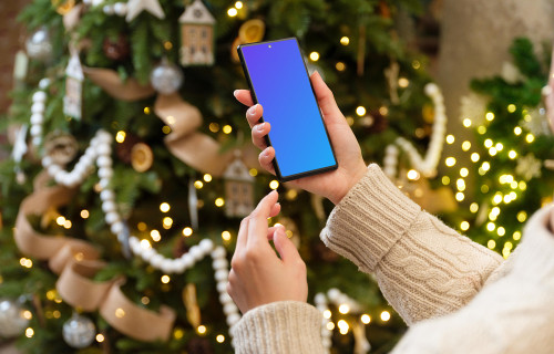 Woman hand holding a smartphone next to the Christmas tree